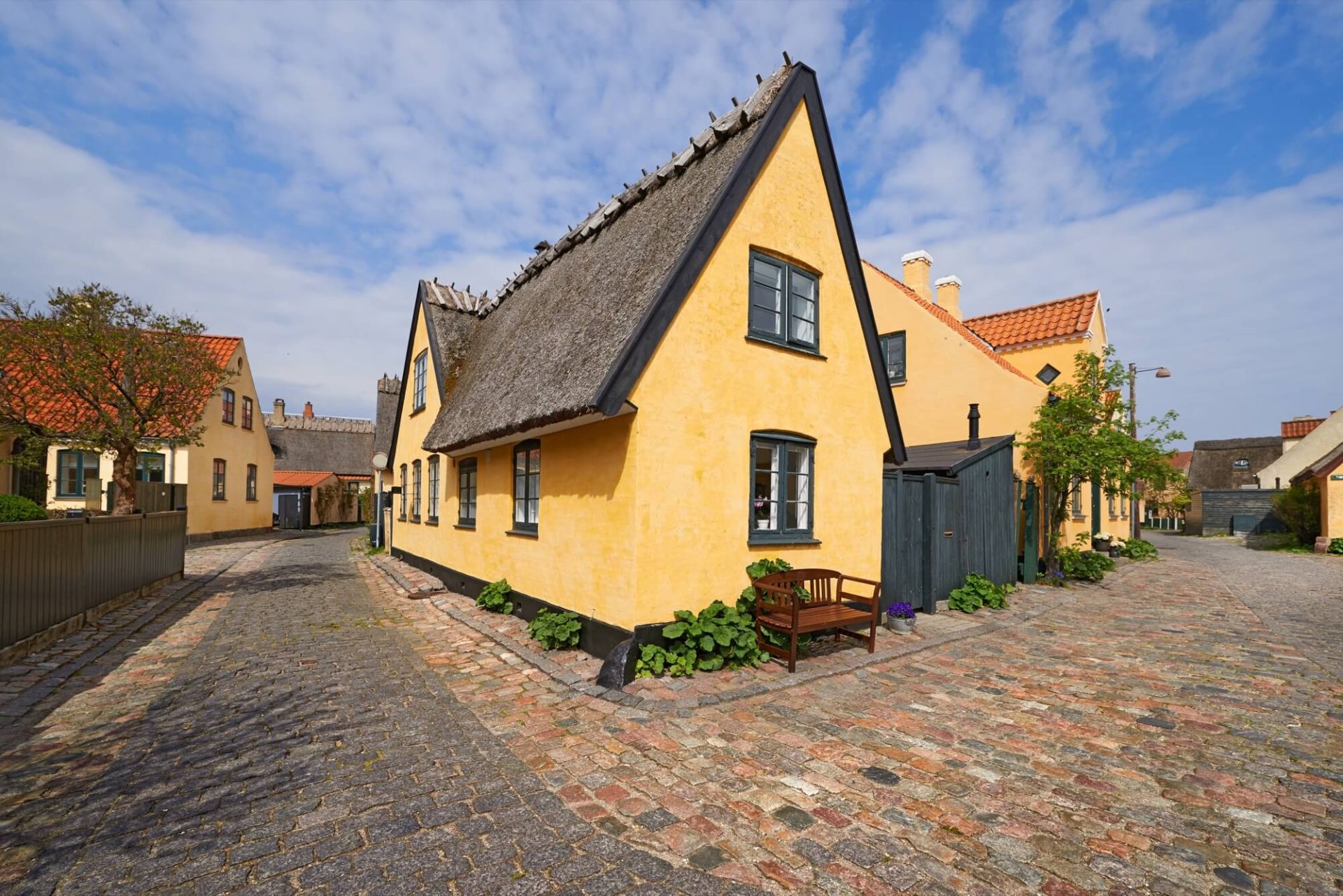 En gatubild förgylls av ett hus med traditionell charm, vars gulputsade fasad kompletteras av svartmålade fönster och ett naturligt halmtak